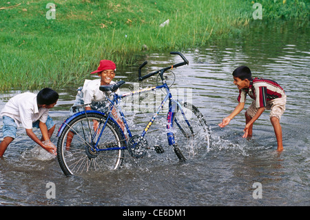 Indian children boys washing cleaning bicycle with water in pond ; India ; Asia Stock Photo