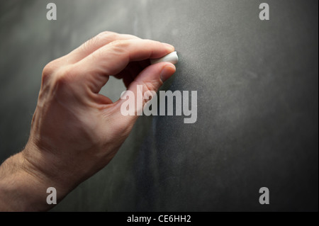 A man male teacher left hand writes using chalk on a chalkboard blackboard. Stock Photo