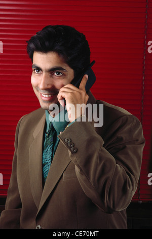 DPA 84055 : South Asian Indian executive man brown jacket green shirt tie talking mobile phone red blinds MR#139 Stock Photo