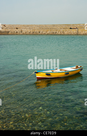 A bright yellow colourful boat in a clear turquoise sea, behind is the harbour wall and blue sky. St MIchaels Mount, Cornwall Uk Stock Photo
