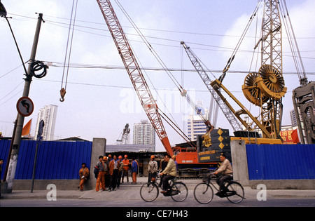 Bicyclers pass by a construction site in the city of Shanghai China Stock Photo