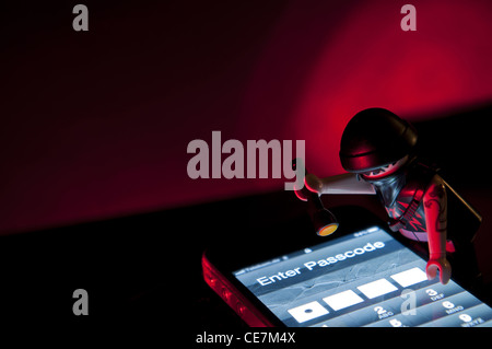 Playmobil Hacker dressed in dark clothing with torch about to steal information from mobile. Stock Photo