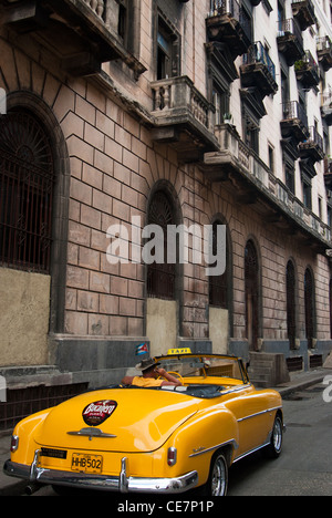 old American car used as taxi with a driver on his mobile phone wearing a cowboy hat. Bucanero advert on the car. Cuban flag Stock Photo