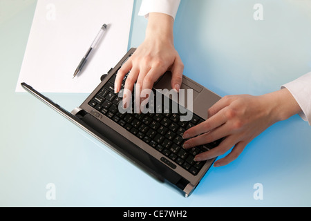 Woman's hand gently enters data in a netbook readu to make notes on an empty sheet of paper Stock Photo