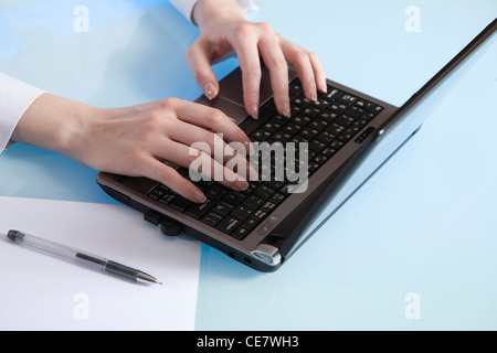 Woman's hand gently enters data in a netbook readu to make notes on an empty sheet of paper Stock Photo