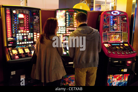 A young couple playing on the slot machines in the amusement arcade, Cambridge UK Stock Photo