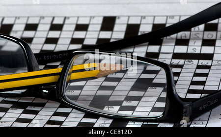 A pair of reading glasses lying upturned on top of a large incomplete crossword with a pencil Stock Photo