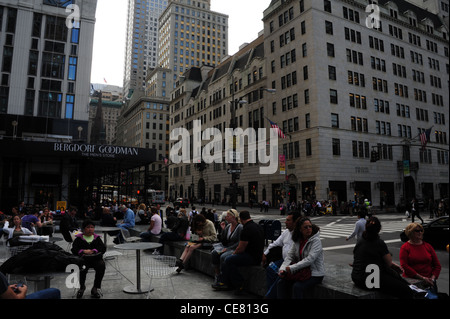 Grey sky view people sitting relaxing tables chairs Apple Store pedestrian plaza, 5th Avenue towards East 58th Street, New York Stock Photo