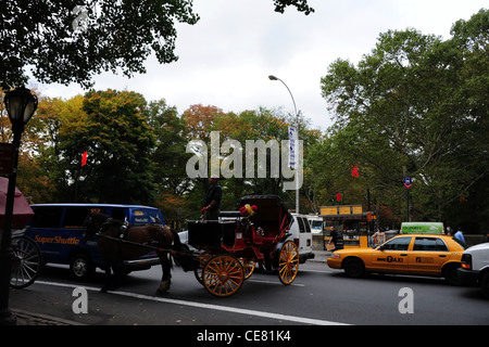 Autumn trees view yellow taxi blue van, black horse-drawn carriage turning round, Grand Army Plaza, Central Park South, New York Stock Photo