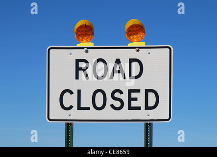 Road closed sign with orange lights against a bright blue sky Stock Photo