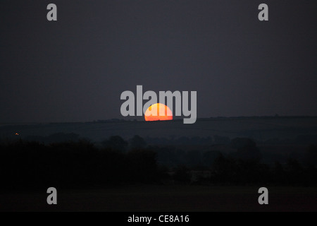 nearly full moon rising over horizon in the early evening light Stock Photo