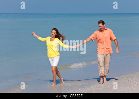 Man and woman romantic couple running holding hands on a deserted tropical beach with bright clear blue sky Stock Photo