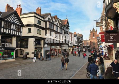 Busy pedestrianised cobbled street scene with shops in historic Tudor buildings in city town centre. Bridge Street Chester Cheshire England UK. Stock Photo