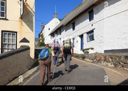 Group of walkers walking up steep hill through narrow village street with white cottages in Cadgwith Cornwall England UK Britain Stock Photo