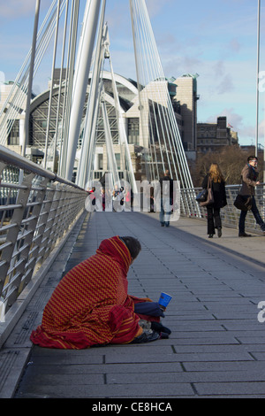 man wrapped in blanket begging on Golden Jubilee Bridge, London, UK Stock Photo