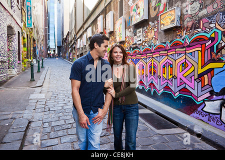 Young couple walking in city laneway, holding hands and looking at street art. Hosier Lane, Melbourne, Victoria, Australia Stock Photo