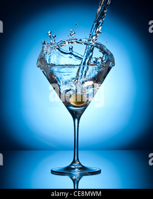 Splash martini from flying olives. Object on a blue background. Stock Photo