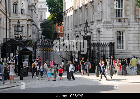 Tourists on pavement outside Downing Street in front of steel security gates controlled by armed Metropolitan police officers in London England UK