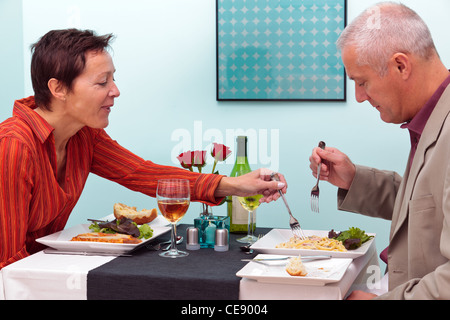 Photo of a mature couple dining in a restaurant, she is trying his pasta dish. Stock Photo