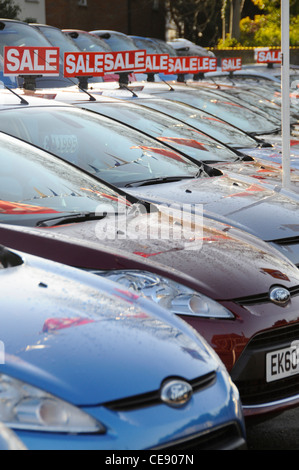 Long line of used second hand pre owned motor cars for sale on Ford car dealership forecourt with red sale signs above windscreens Essex England UK