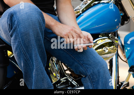 USA, Illinois, Metamora, midsection of man sitting on bike and texting on phone Stock Photo