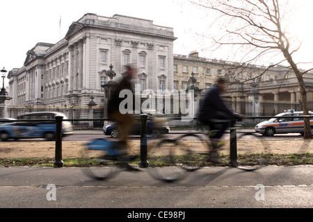 Buckingham Palace with two cyclists riding passed in the foreground and traffic in the background Stock Photo