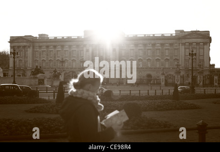 Buckingham Palace with a lady reading tourist information in the foreground as she walks passed Stock Photo