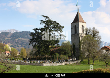 View of the church and cemetery on the alpine hill. In the background are peaks of the Alps. Spring in Switzerland. Stock Photo