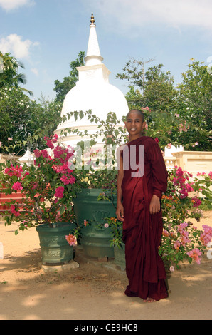 A young Buddhist Monk dressed in traditional red robes stands infront of the temple at his Monastary Stock Photo
