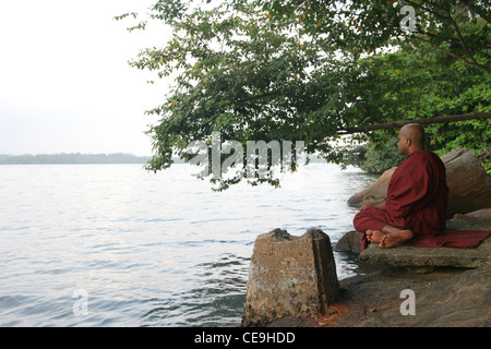 A monk at a Buddhist temple meditates infront of a large lake Stock Photo