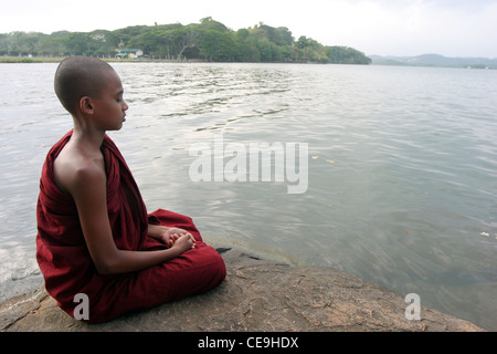 A young monk at a Buddhist temple meditates infront of a large lake Stock Photo