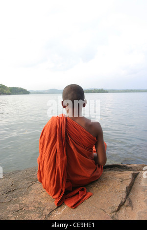 A young monk at a Buddhist temple meditates infront of a large lake Stock Photo