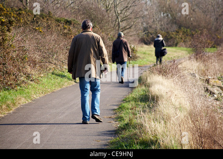 Three people walking along footpath at Holes Bay, Poole in January Stock Photo