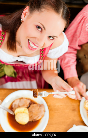 Inn or pub in Bavaria - couple in traditional Tracht drinking beer and eating roast pork with dumplings Stock Photo
