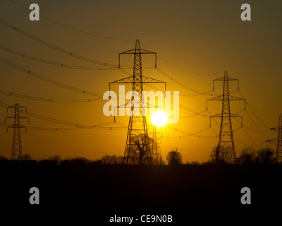 The sun, setting behind electrical pylons in the countryside. Stock Photo