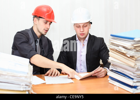 Architect and construction engineer discussing plan in office room. Caucasian people in helmets Stock Photo