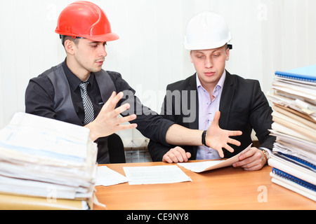 Architect and construction engineer discussing plan in office room. Caucasian people in helmets Stock Photo