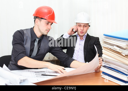 Architect and construction engineer discussing plan in office room. Caucasian people in helmets Stock Photo