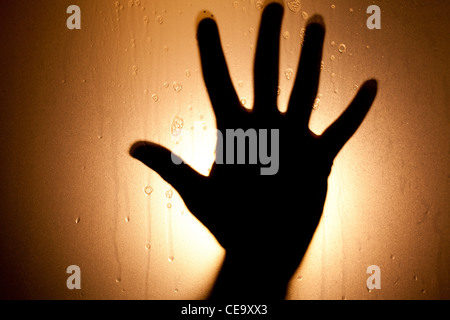 Fear under the shower. Back lighted hand behind glass with foam and water drops Stock Photo