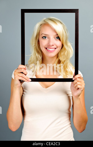 Portrait of smiling young woman holding picture frame on grey background Stock Photo