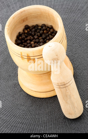 wood mortar and pestle full with aromatic black peppercorns Stock Photo