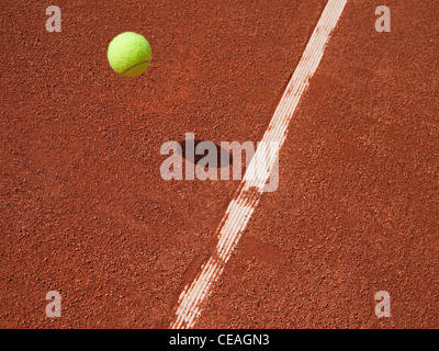 Tennis ball in air approaching the line on a red clay court. Stock Photo