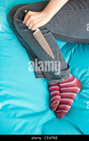 Woman lying down and holding a knife in a firm grip Stock Photo