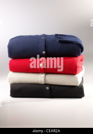 Stack of four folded knitted cardigans in navy blue, red, cream and black on a white background. Stock Photo