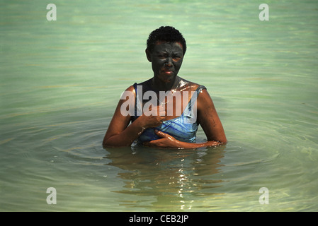 A tourist from Africa smeared with natural black mud from the Dead Sea bathing at the shore of the Dead Sea in Israel Stock Photo