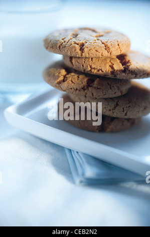 Ginger snap cookies (biscuits) served with a glass of milk on white table-ware. Stock Photo