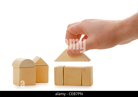 The hand establishes a toy roof on wooden cubes. Isolated on white Stock Photo