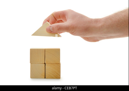 The hand establishes a toy roof on wooden cubes. Isolated on white Stock Photo