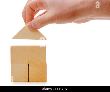 The hand establishes a toy roof on wooden cubes. Isolated on white Stock Photo