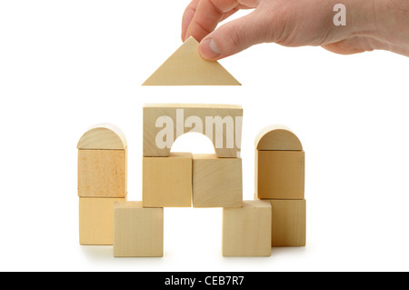 The hand establishes a toy roof on wooden cubes. Isolated on white Stock Photo